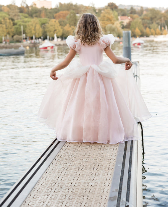 Young girl wearing a light pink princess ball gown on a waterfront dock
