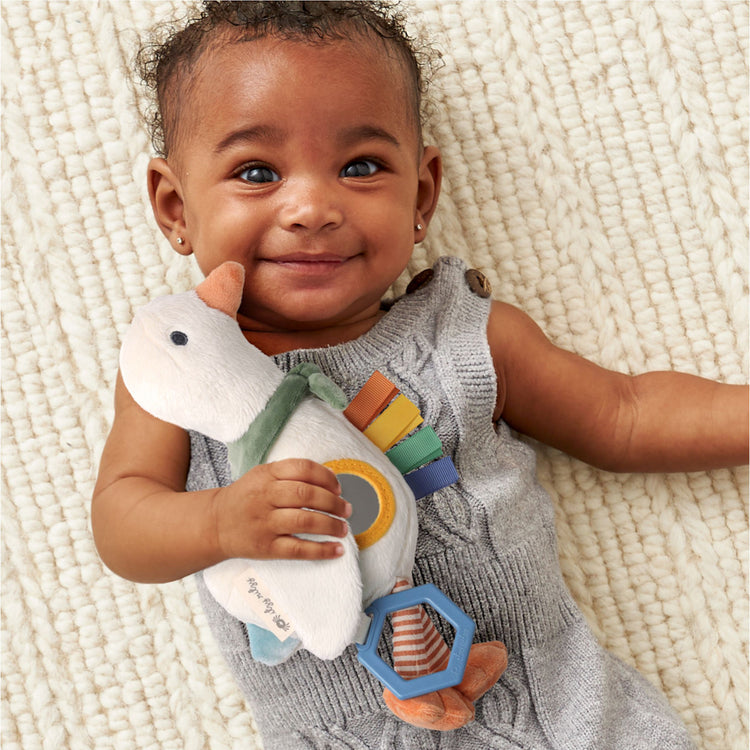 Smiling baby holding Itzy Ritzy Bitzy Traveler Goose plush sensory toy with teether