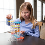 Young girl placing a marble into a tall colorful Trestle Track Pro marble run tower on a table.
