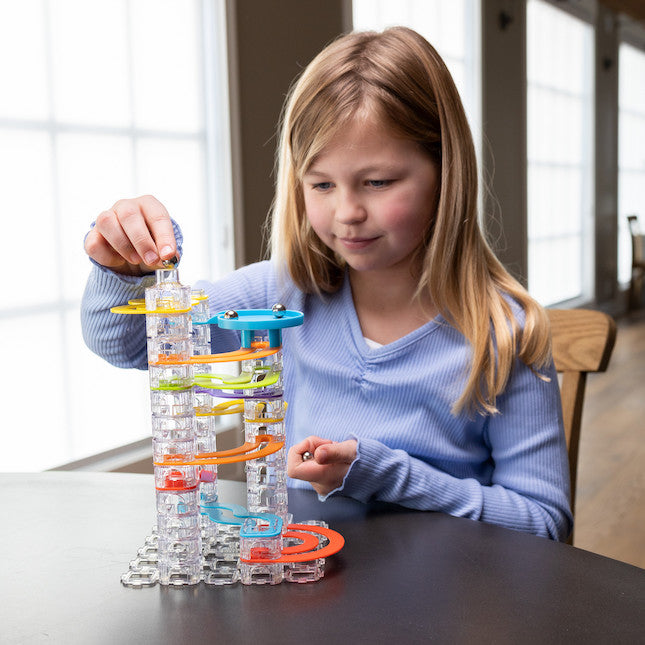 Young girl placing a marble into a tall colorful Trestle Track Pro marble run tower on a table.