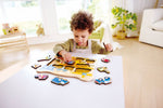 Young toddler playing with Hape construction vehicles wooden peg puzzle on white table