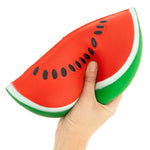 Hand holding a jumbo watermelon slice squishy toy with black seeds on white background