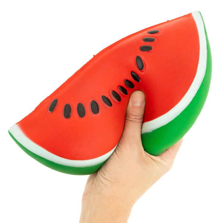 Hand holding a jumbo watermelon slice squishy toy with black seeds on white background