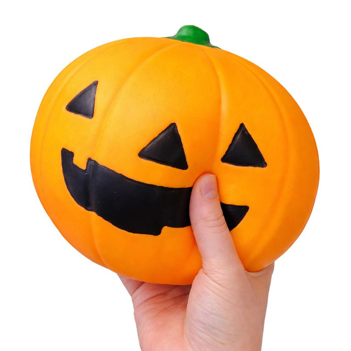 Hand squeezing an orange jack-o-lantern squishy toy with smiling face and green stem