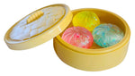 Yellow dumpling steamer basket toy containing three colorful glittery squishy dumpling stress balls