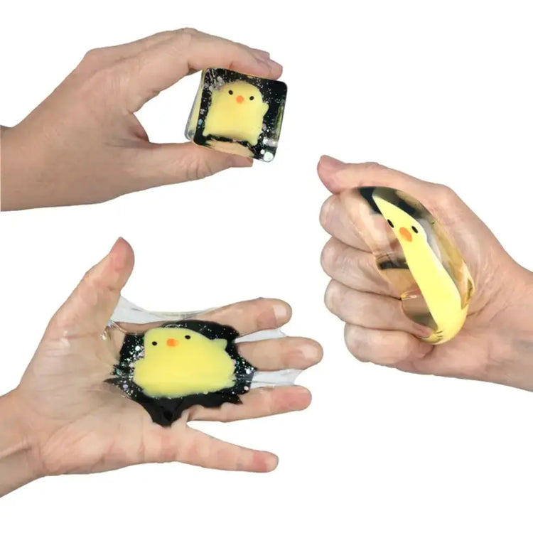 Hands squishing and stretching a black glow-in-the-dark cube toy containing a yellow chick figure