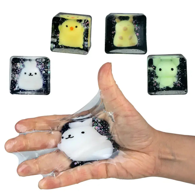 Hand squishing a black glitter cube toy with cute white animal mochi figure inside
