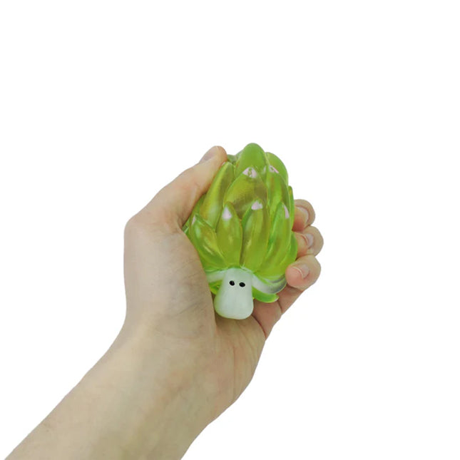 Hand squeezing a green leaf sheep-shaped squishy toy against white background